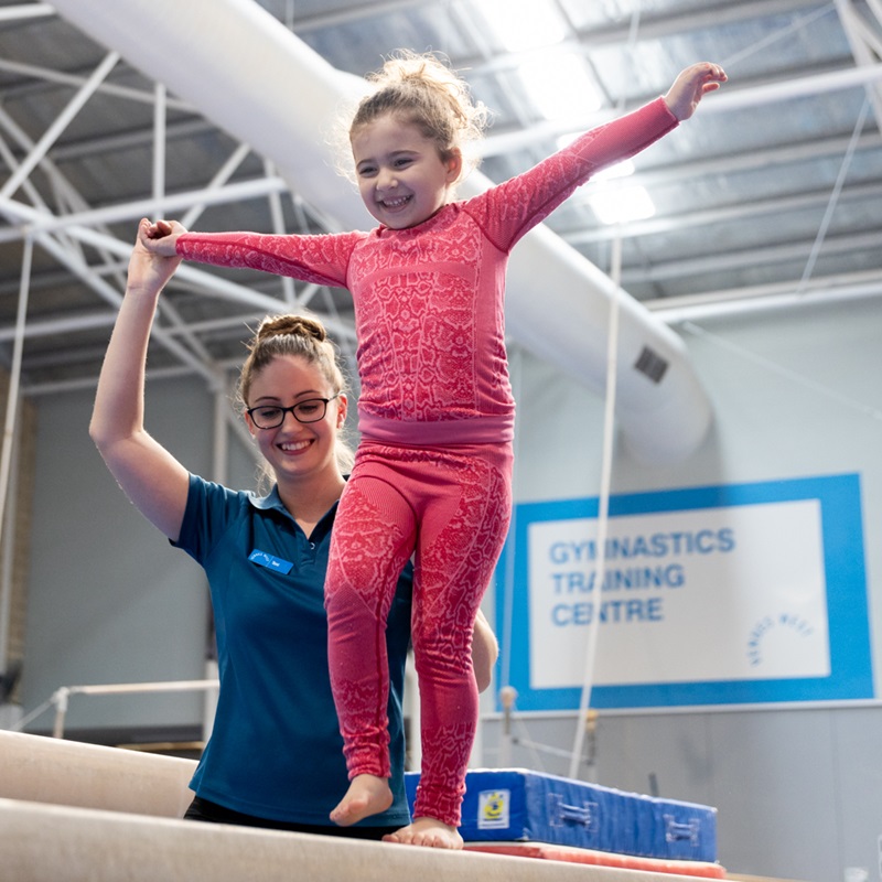 Gymnastics coach assisting a young girl walk on the balance beam