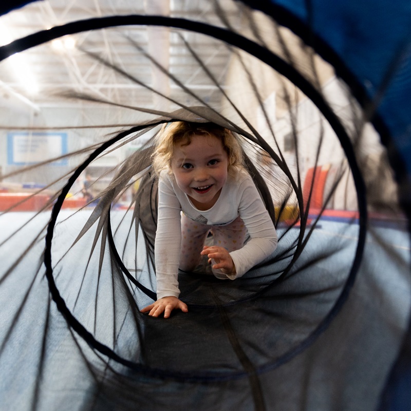 Young girl climbing through play tunnel at kindy gym