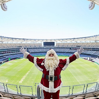 Photo of a person in a Santa suit in the Optus Stadium stands with the field behind them in Burswood, Perth